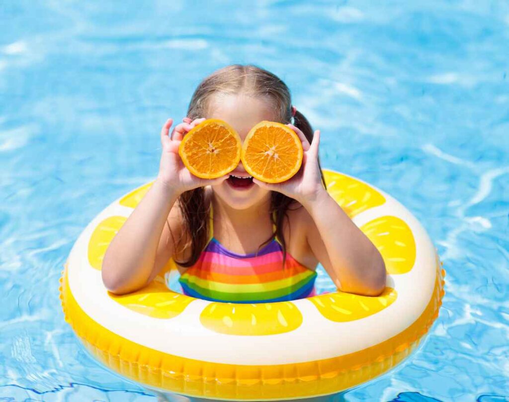 Child with pool float holding oranges in front of eyes. Chlorine vs. saltwater pools.